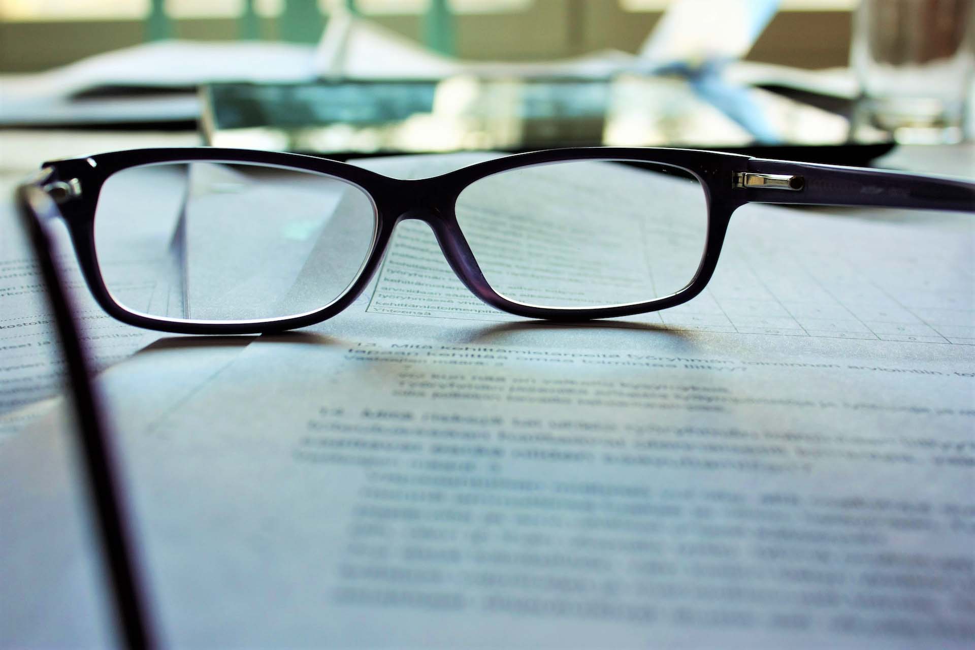 A closeup image of black-framed glasses on a pile of papers with blue in the background
