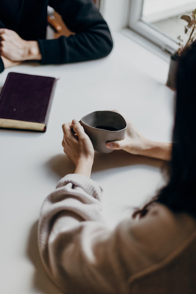 Two people sitting opposite each other at a table with a book and a cup of coffee between them