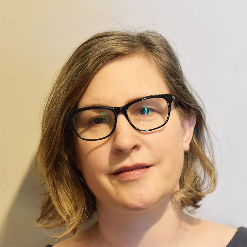 A white woman with brown hair wearing black-framed glasses